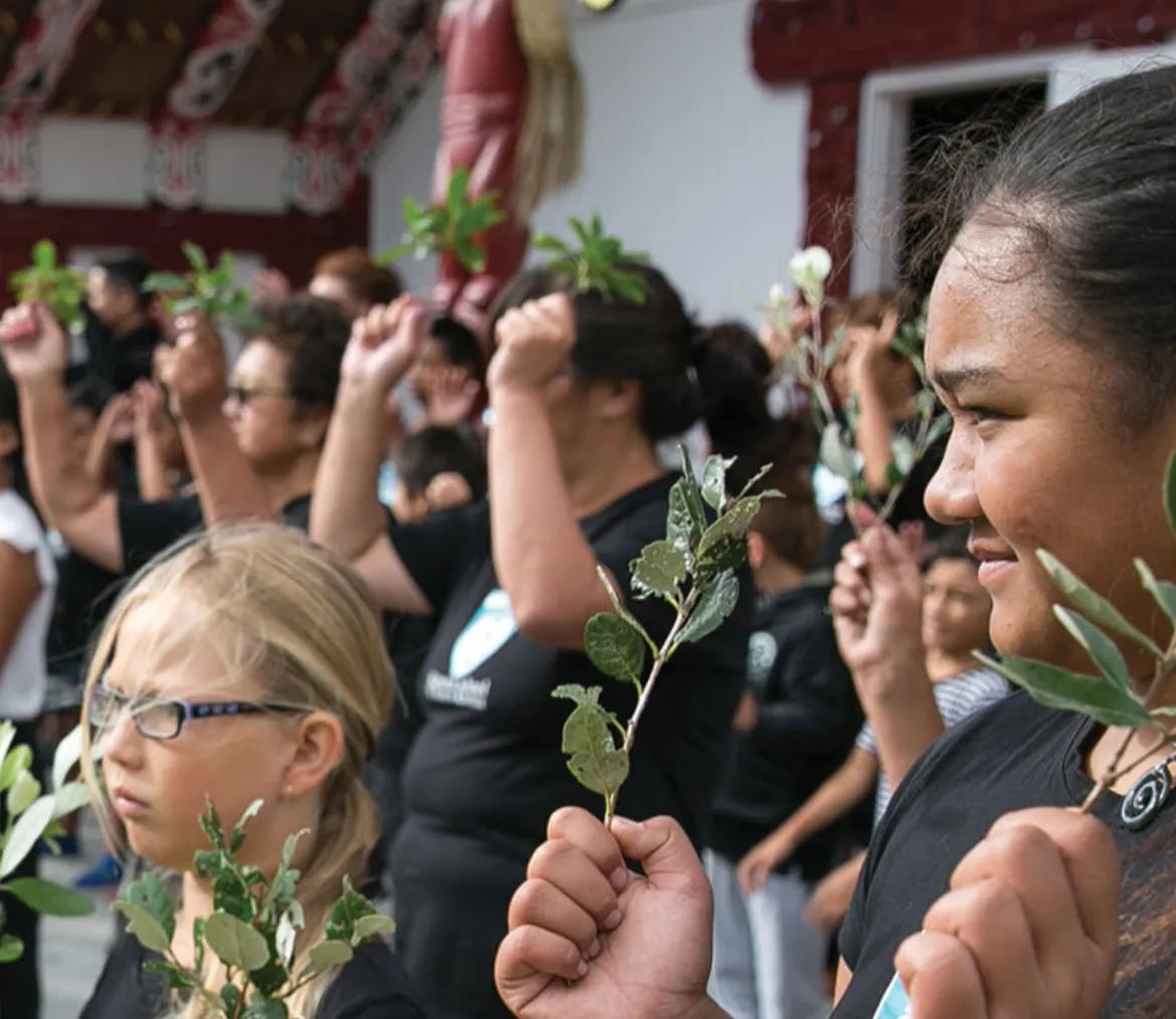 People holding leafy branches at the 2018 Poukai ceremony at Maketu Marae