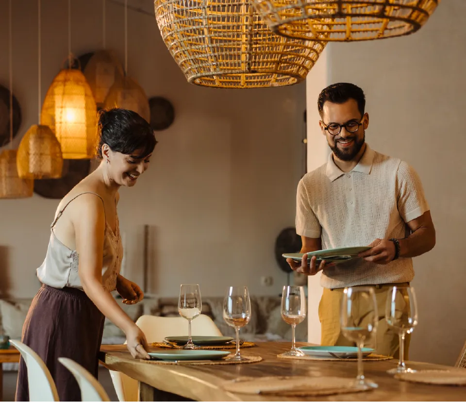 Couple setting a dining table beneath woven pendant lights