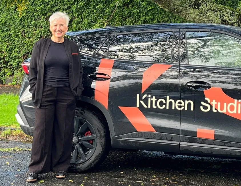 Kitchen Studio team member standing beside a branded black vehicle